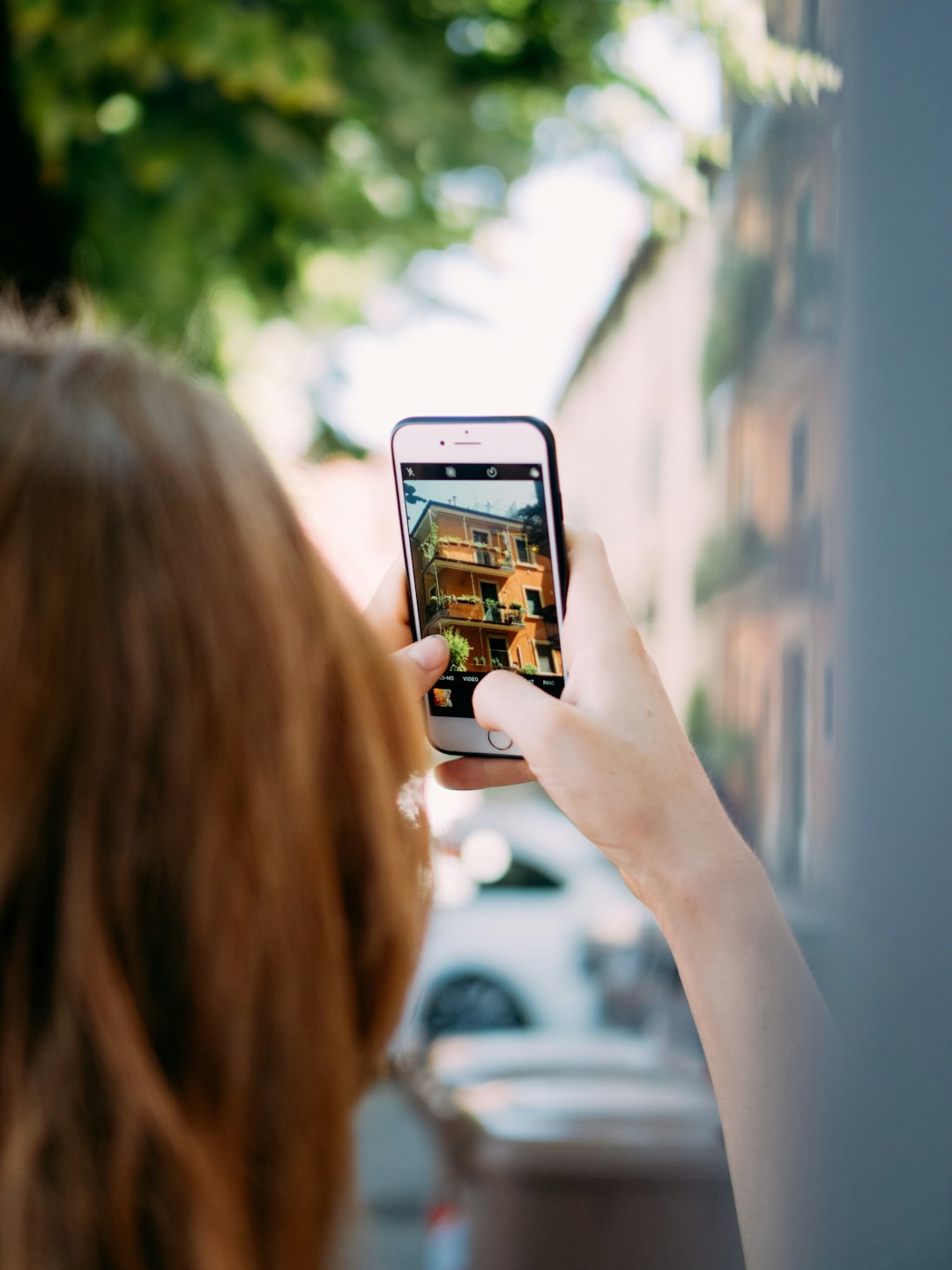 Person holding a smartphone to photograph an orange building with plants.